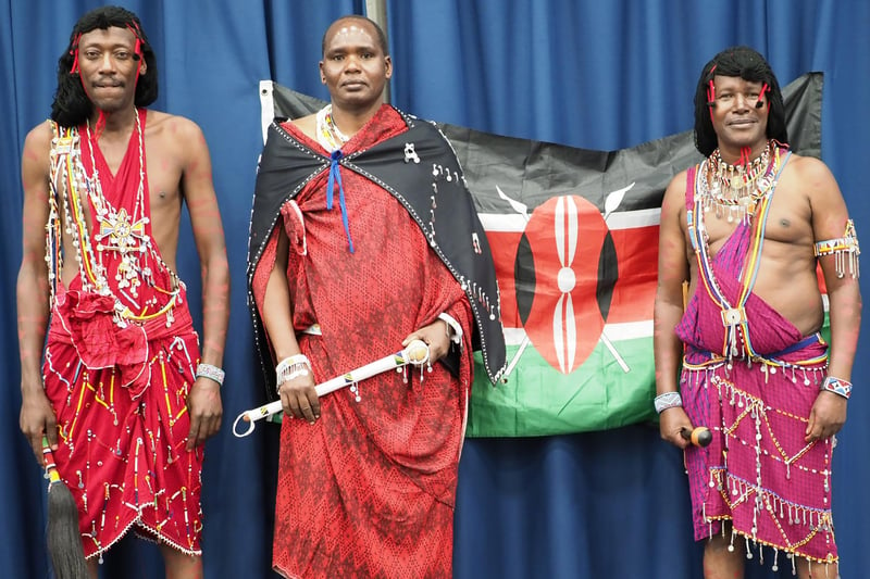 Men dressed in traditional tribal clothing in front of the Kenyan flag