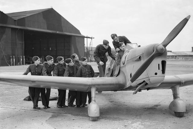 Men in uniform stand next to a war plane
