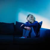 A woman sitting with her arms around her knees in a dark room. Picture: Dominic Lipinski via PA Images / Alamy Stock Photo