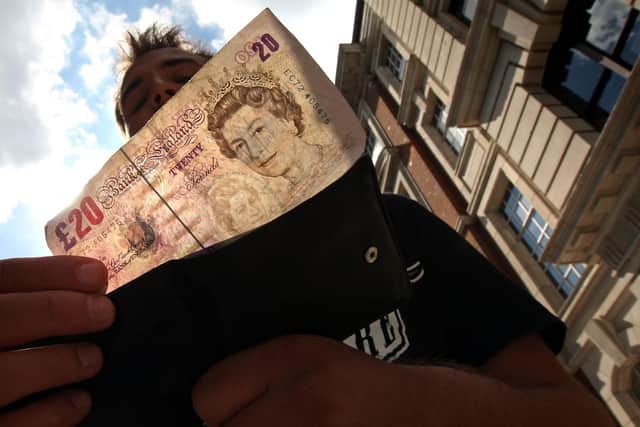 A man takes a 20 pound note from his wallet outside a bank. Photo by Cate Gillon/Getty Images